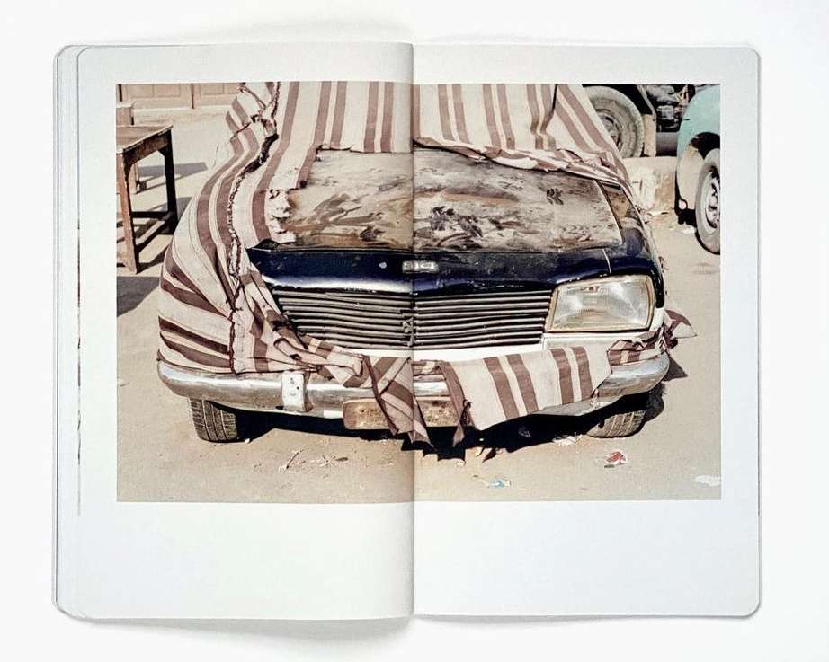 Photograph of a black vehicle partially covered by a striped cloth, captured indoors within the pages of a photography book.