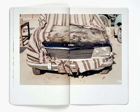 Photograph of a black vehicle partially covered by a striped cloth, captured indoors within the pages of a photography book.
