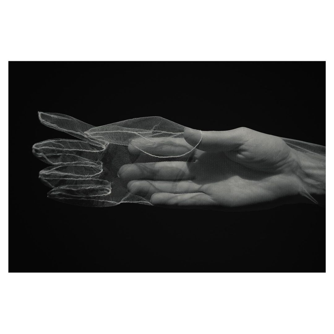 A hand with sheer white fabric overlay against a stark black background, showcasing texture and monochrome contrast for a dramatic visual.