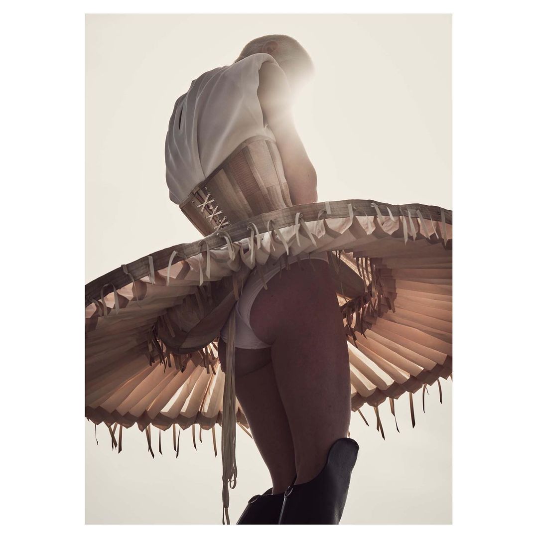 Backlit fashion shot of a woman wearing a corset, skirt, and boots, the flared skirt lit by sunlight from behind, creating a halo effect.