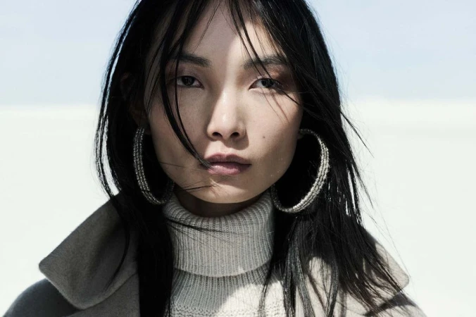 Close-up portrait of an east asian woman wearing a turtleneck sweater and large hoop earrings by Alistair Taylor-Young