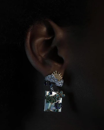 Close-up of a person wearing an elaborate jewelled cloud and tree earring photographed by Alistair Taylor-Young.