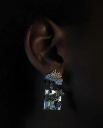 Close-up of a person wearing an elaborate jewelled cloud and tree earring photographed by Alistair Taylor-Young.