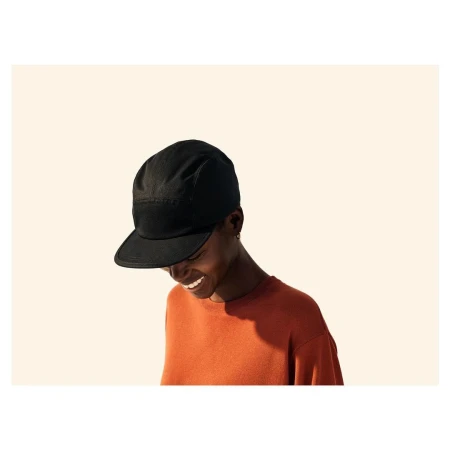Smiling person wearing a black cap and orange sweater against a plain light background