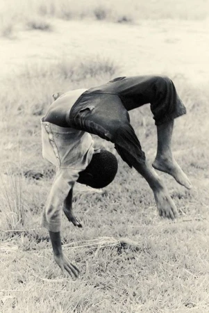 Monochrome photograph by Alistair Taylor-Young capturing a young boy doing a backbend in a grassy field.