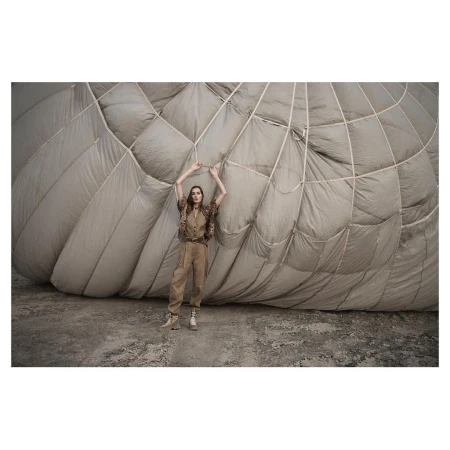 Model standing in front of a giant deflated hot air balloon wearing beige utility trousers and patterned short-sleeve shirt