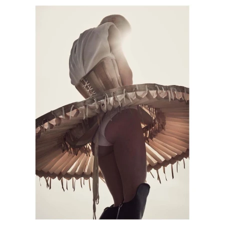 Model wearing a structured corset and wide pleated skirt viewed from a low angle against a bright sky