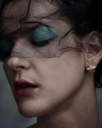 Close-up portrait of a woman wearing a black netted veil, turquoise eyeshadow, and a star-shaped earring, photographed by Alistair Taylor-Young.