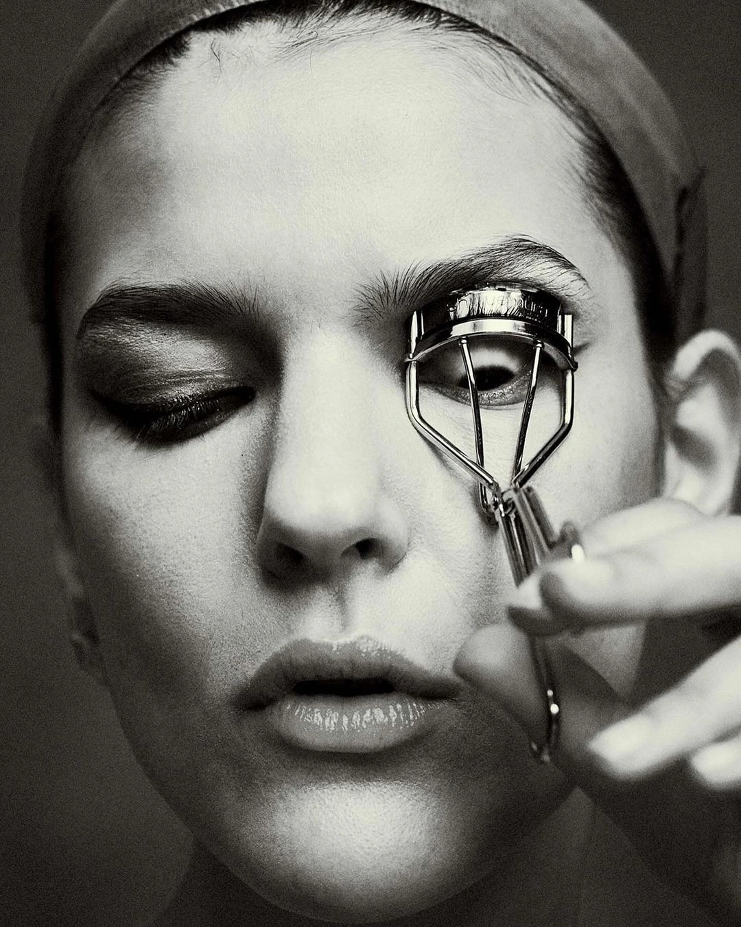 Close-up black and white portrait of a woman using an eyelash curler by photographer Alistair Taylor-Young.