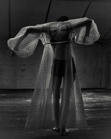Model from behind wearing a sheer polka dot robe with dramatic balloon sleeves in a moody industrial interior.