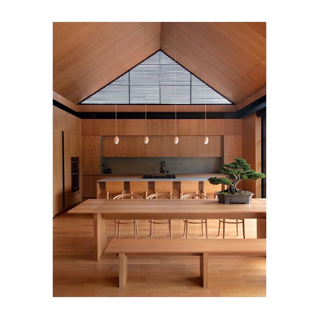 Interior design featuring a dining table with a bonsai tree, wooden chairs, light wood walls, and ceiling with a triangular window.