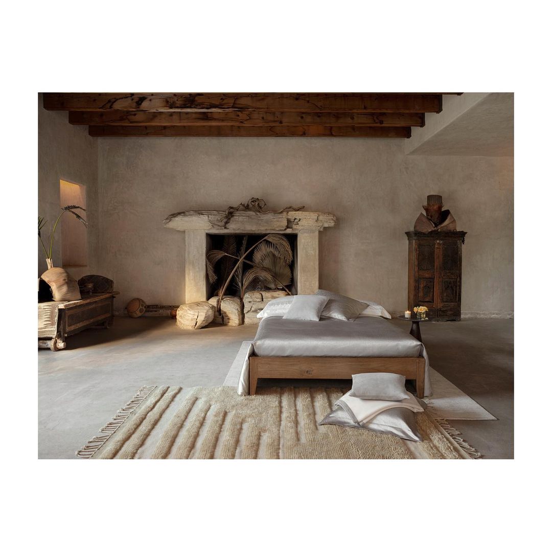 Interior photo showcasing a neatly made bed with pillows and a rug, set against a wall with a faux fireplace and decorative objects.