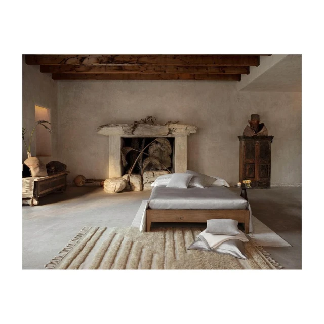 Interior photo showcasing a neatly made bed with pillows and a rug, set against a wall with a faux fireplace and decorative objects.