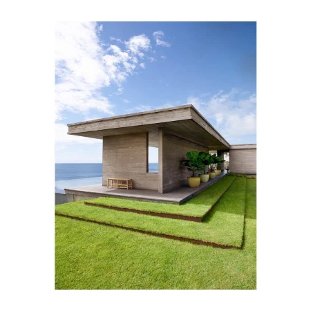 Modern architecture featuring a concrete house with green grass steps leading to an ocean view under a blue sky with clouds.