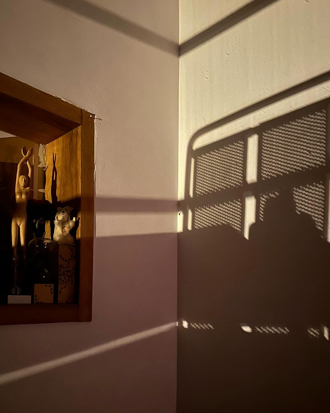 Art display with wooden sculpture and various objects casting shadows on the walls in an indoor setting with warm lighting.