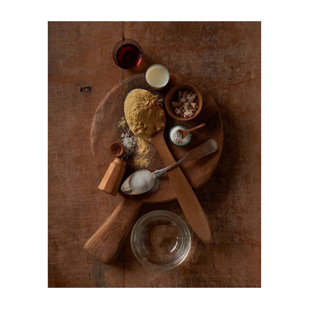 Overhead shot of cornmeal, flour, and various baking ingredients arranged on a wood cutting board and table, food photography.