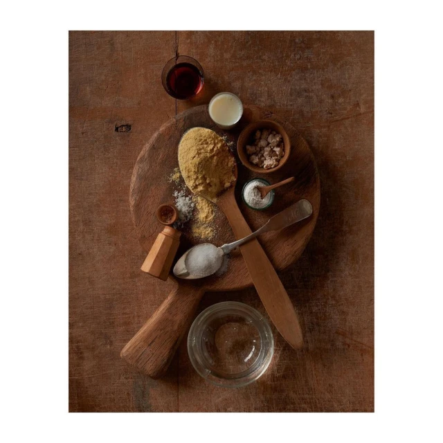 Overhead shot of cornmeal, flour, and various baking ingredients arranged on a wood cutting board and table, food photography.