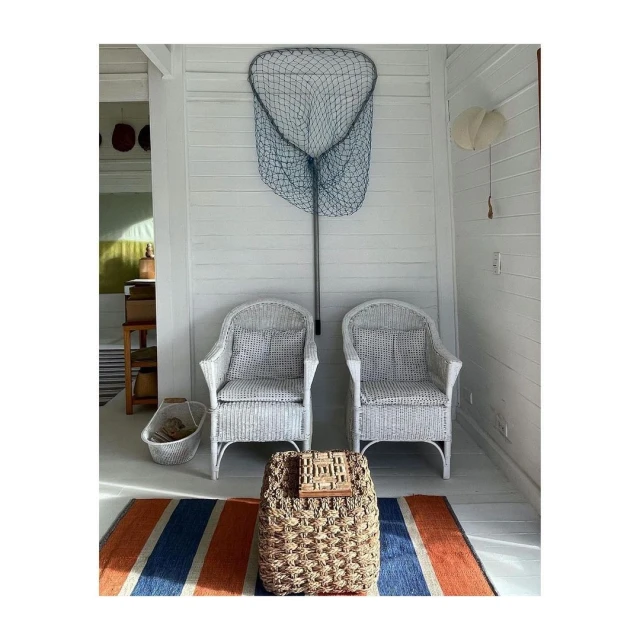 White wicker chairs and a fishing net create a bright, clean interior. Woven ottoman and striped rug add texture and color.