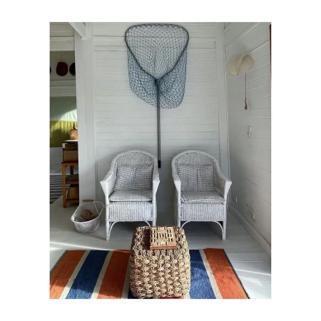 White wicker chairs and a fishing net create a bright, clean interior. Woven ottoman and striped rug add texture and color.
