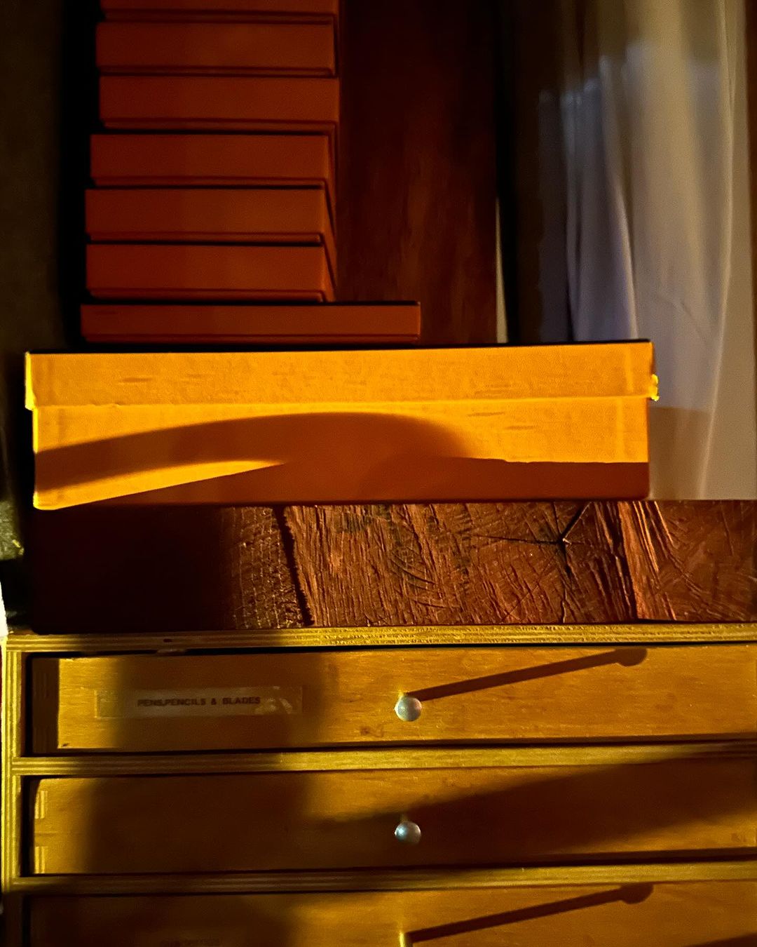 Stacked orange boxes create a visually striking display atop a wood cabinet with drawers in an indoor setting with warm lighting.