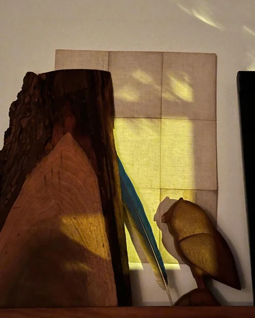 Still life with a wood carving, a feather, and a collage piece. Earth-toned colors and natural textures create a warm, artistic ambiance.