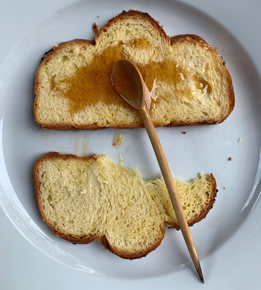Overhead shot of two slices of brioche bread drizzled with honey, with a wooden spoon resting on top, on a white plate.