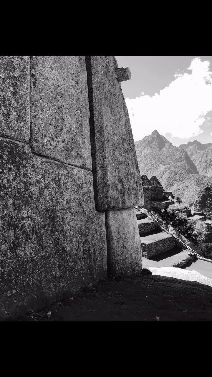 Stone wall leads to mountainous landscape and stairs in a black and white photograph, showing Incan architecture.