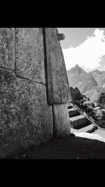 Stone wall leads to mountainous landscape and stairs in a black and white photograph, showing Incan architecture.