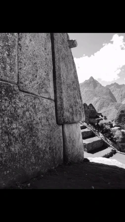 Stone wall leads to mountainous landscape and stairs in a black and white photograph, showing Incan architecture.