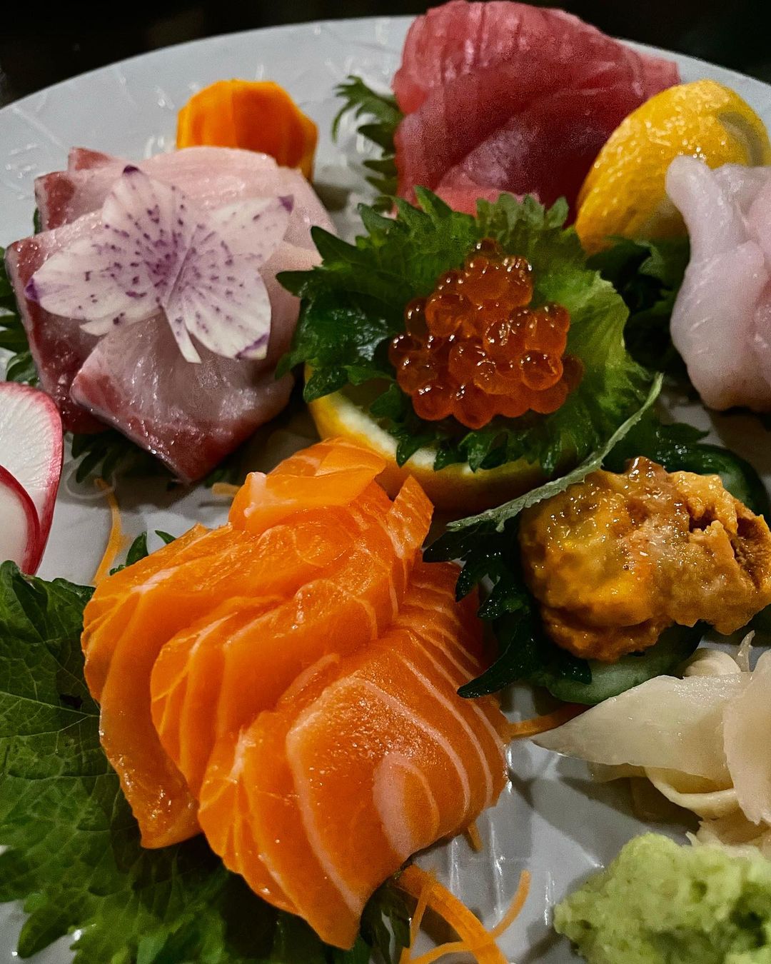 Overhead shot of fresh sashimi assortment featuring tuna, salmon, and assorted seafood delicacies on a white plate with decorative garnishes.