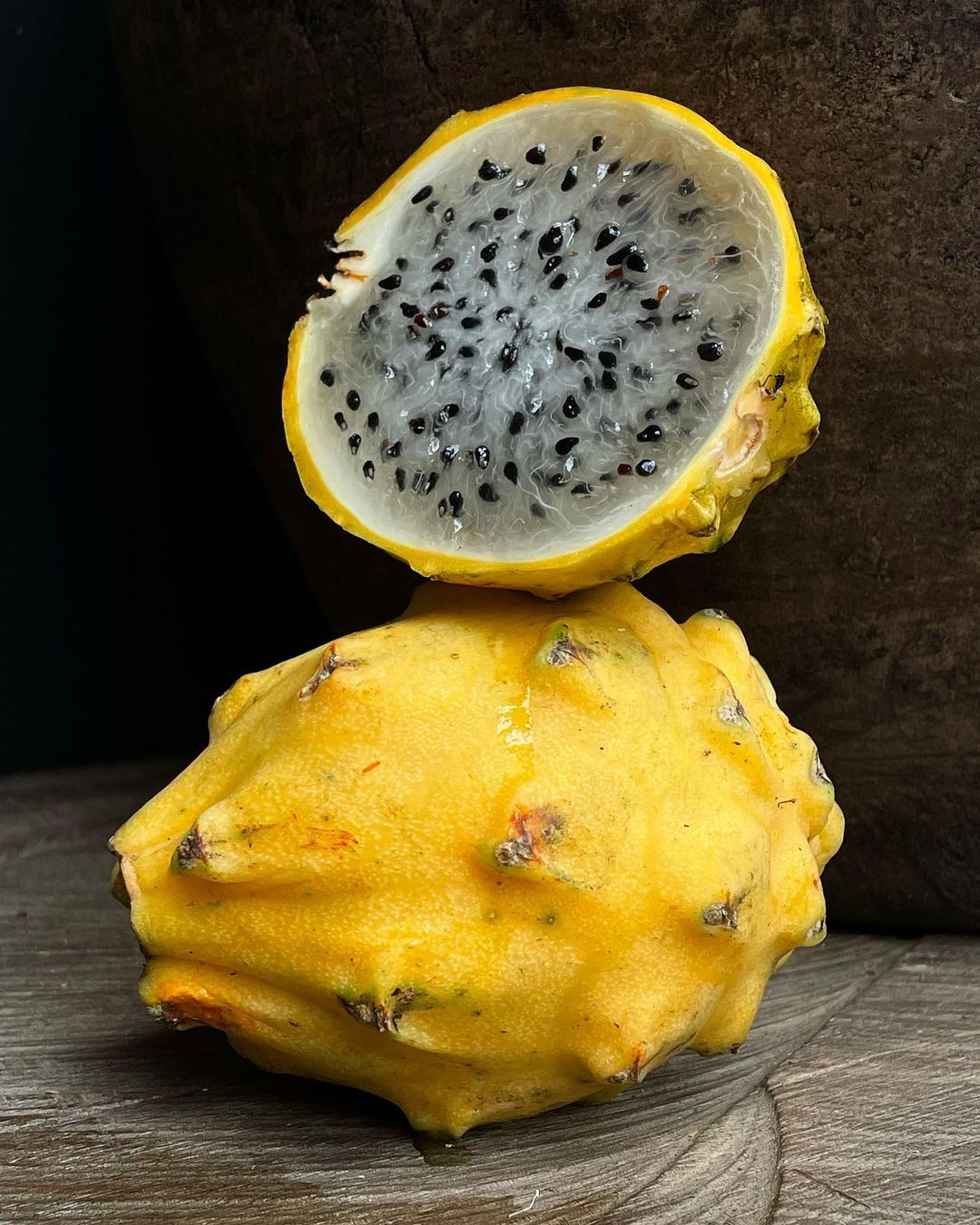Close-up of a halved yellow dragon fruit stacked on top of an intact one, showcasing its white flesh, black seeds, and bumpy skin.