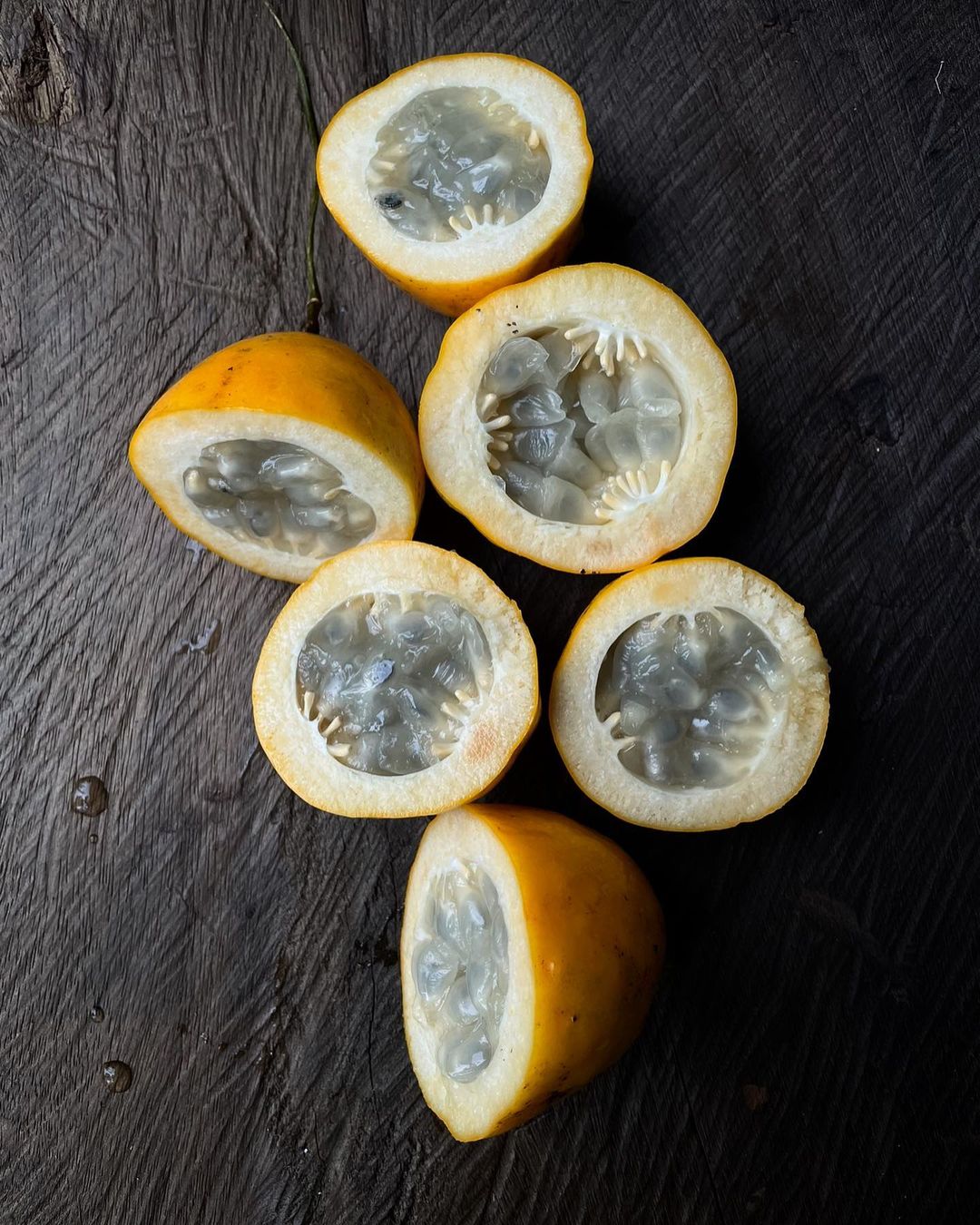 Overhead shot of halved passion fruit sections revealing seeds arranged on a dark wood surface with visible textures and tones.
