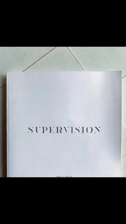 A white softcover book titled 'Supervision' lies on a white surface, shot in soft, natural lighting.