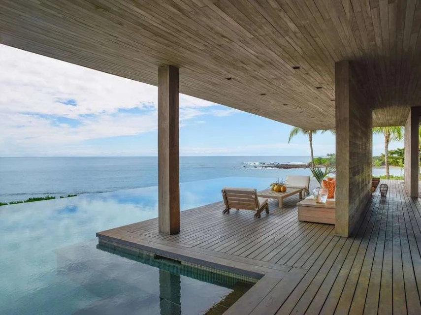 Luxurious modern home with an infinity pool overlooking the ocean, featuring wooden architecture and an inviting outdoor lounge area.