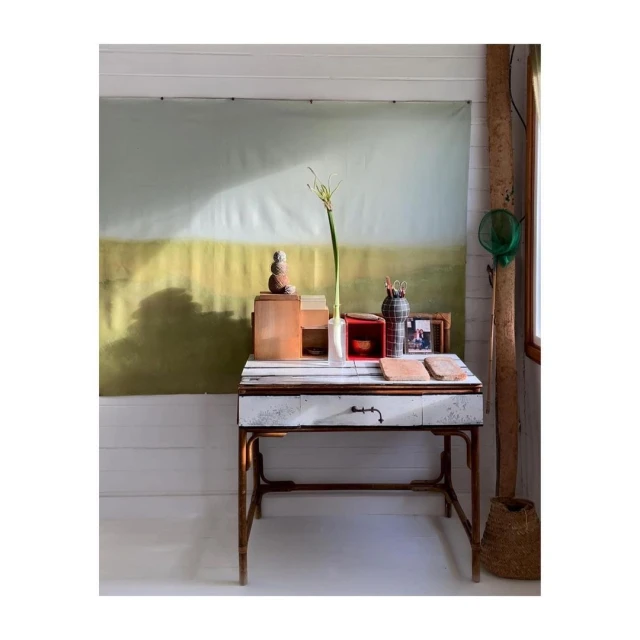 Indoor studio setup featuring a rustic desk with wooden boxes, vases, and a backdrop with a landscape-style painting in soft, muted tones.