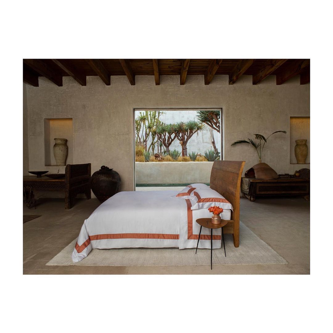 Bedroom interior with white bed, wooden frame, and potted plants visible through a large window, creating a serene and modern aesthetic.