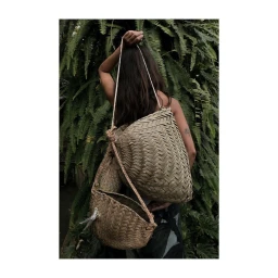 Woman holding woven straw bags against a lush background of green fern leaves