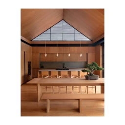 Interior shot of a minimalist wooden kitchen and dining area featuring a bonsai tree on a long dining table by Anita Calero