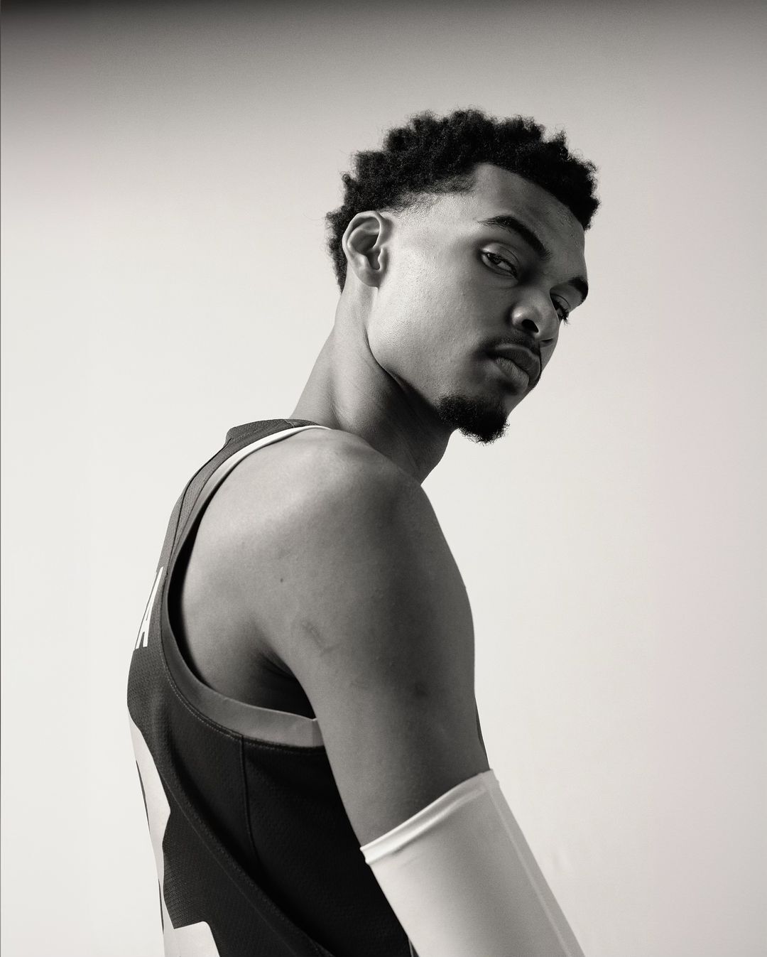 Portrait of a young Black male athlete wearing a jersey and arm sleeve against a plain white background.