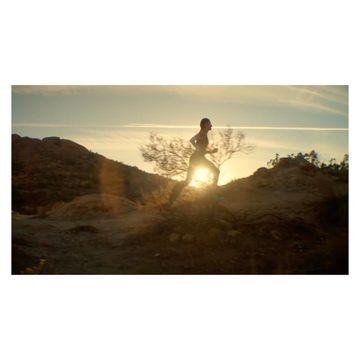 An athletic man runs on a sandy hill at sunset, silhouetted against the sun, showcasing an active lifestyle in a natural environment.