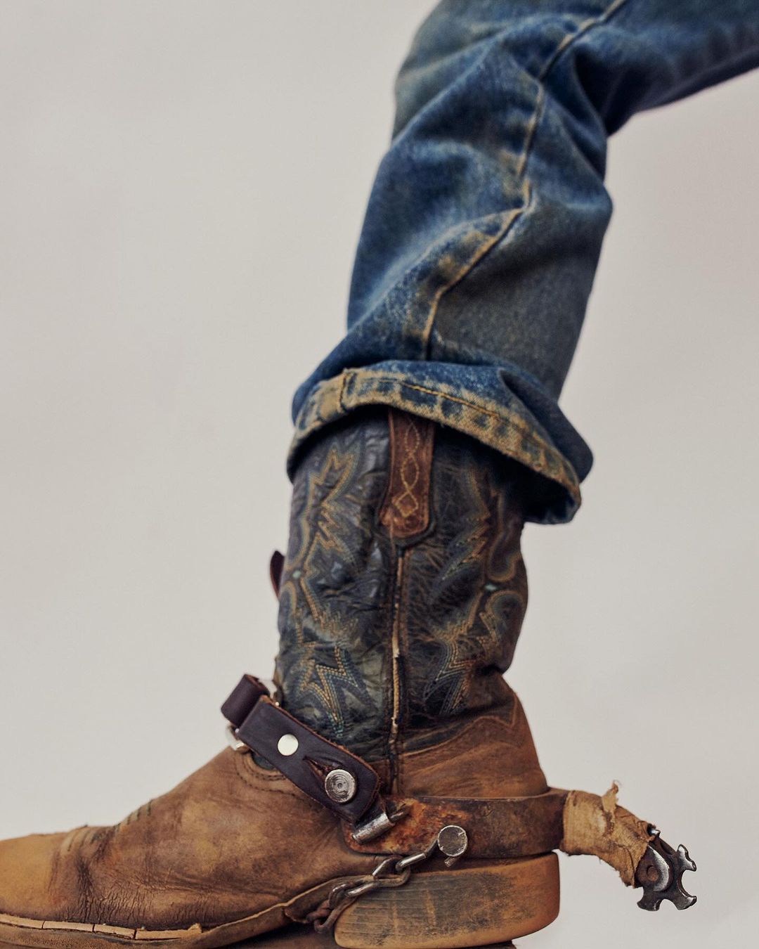 Close-up of cowboy boot and jeans, showcasing the details and texture of the boot and denim in a studio environment.