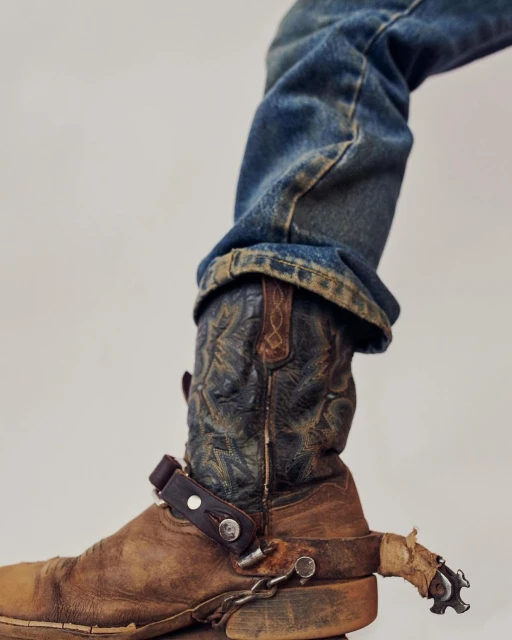 Close-up of cowboy boot and jeans, showcasing the details and texture of the boot and denim in a studio environment.