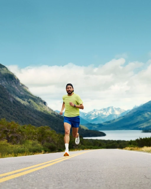 Male runner in athletic wear runs on rural asphalt road with mountains and blue sky in the background, enhancing travel or fitness concept.