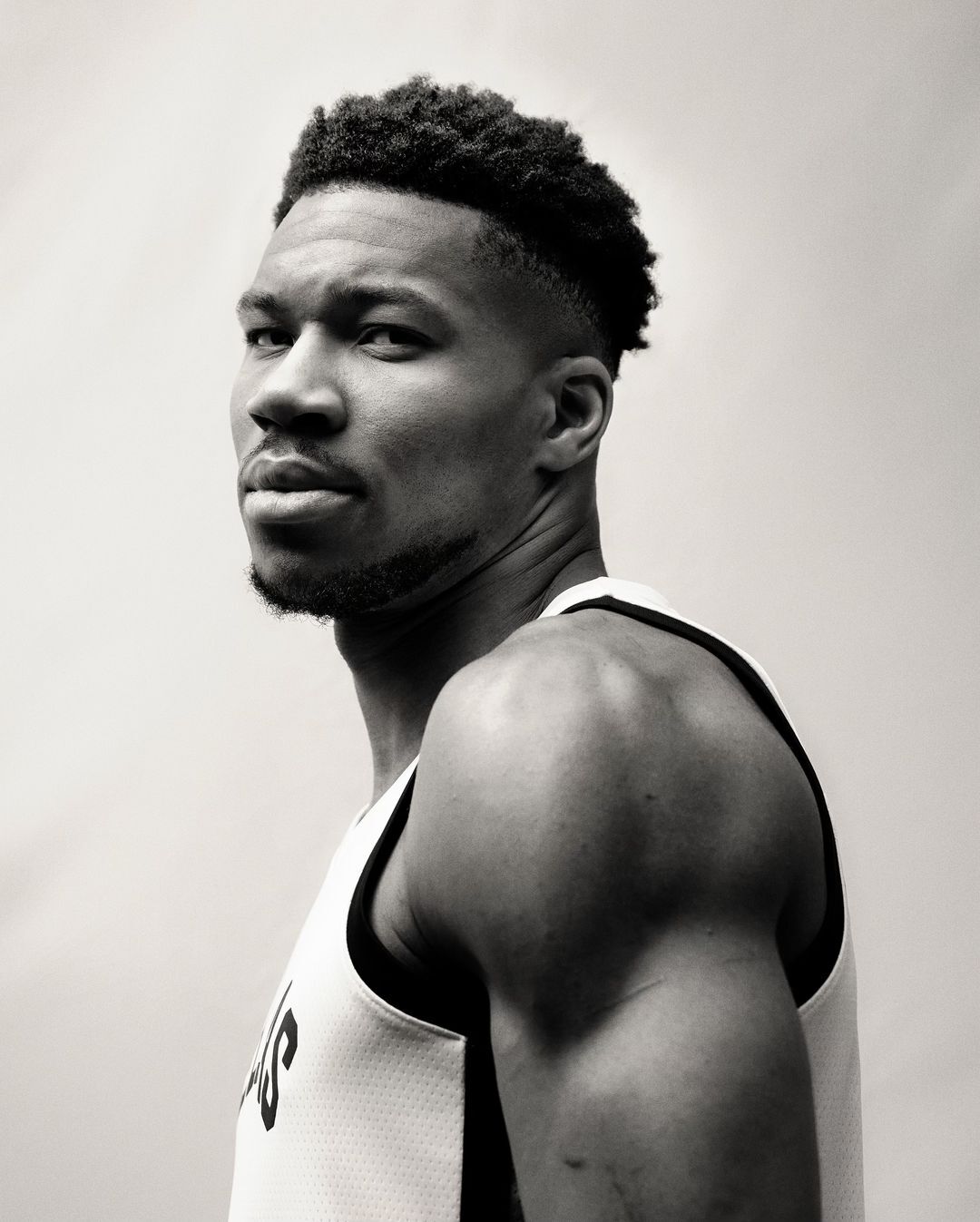 Close-up portrait of a muscular adult male in a sports jersey, looking over his shoulder against a neutral background in black and white.
