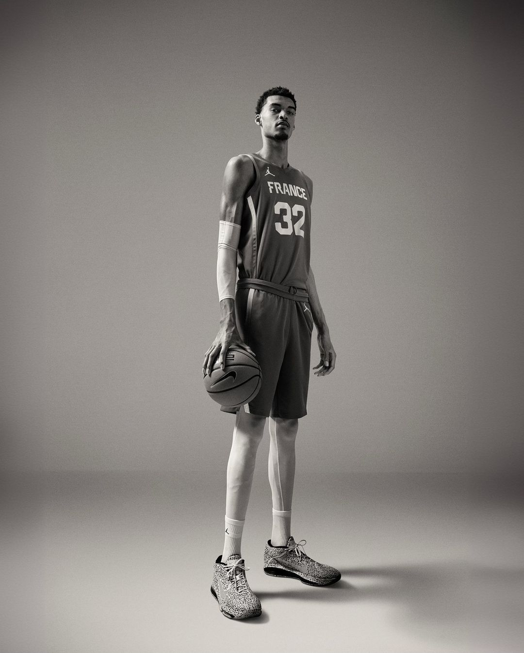 Tall basketball player, Victor Wembanyama, in France jersey holds a basketball in a full-length studio shot.
