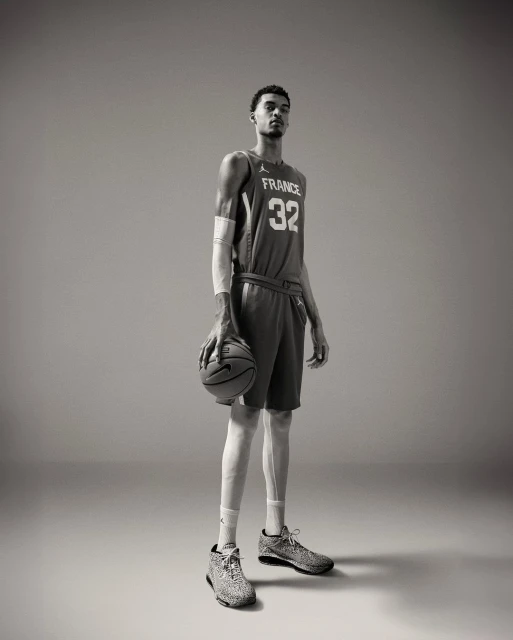 Tall basketball player, Victor Wembanyama, in France jersey holds a basketball in a full-length studio shot. 
