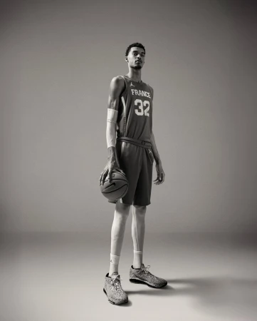 Tall basketball player, Victor Wembanyama, in France jersey holds a basketball in a full-length studio shot. 