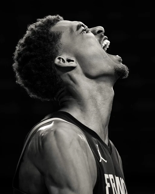 Black and white portrait of a male basketball player with his mouth open, wearing a France jersey with a dark background.