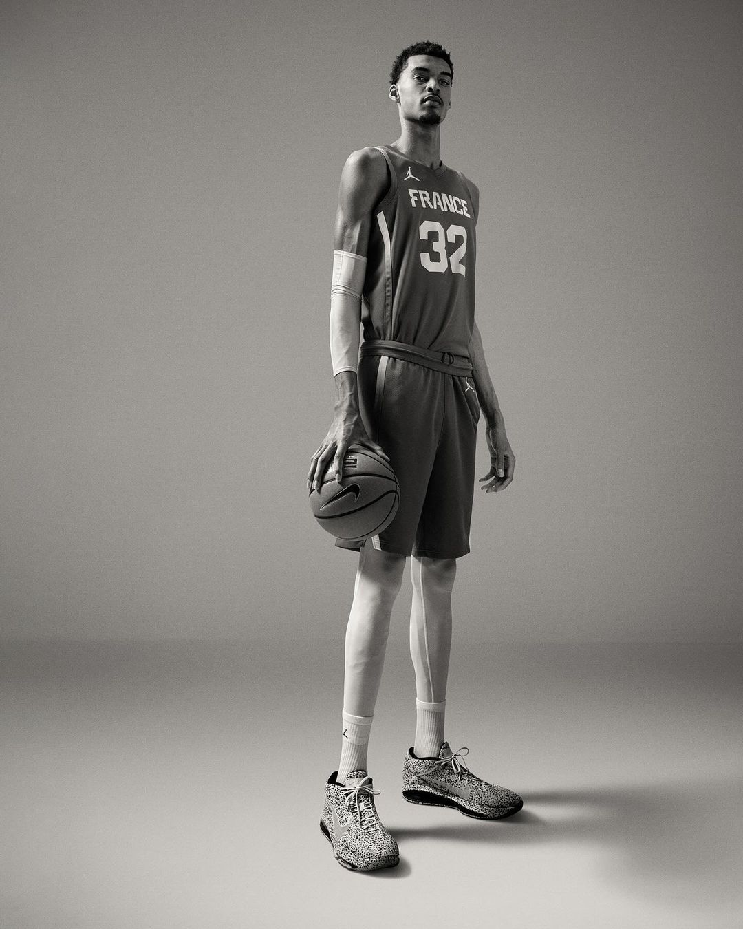 Full-length portrait of tall African-American male athlete in France jersey holding basketball in photo studio with neutral grey background.