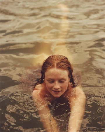 Red-haired woman smiling while swimming in dark water, shot from an elevated angle by Anthony Blasko.